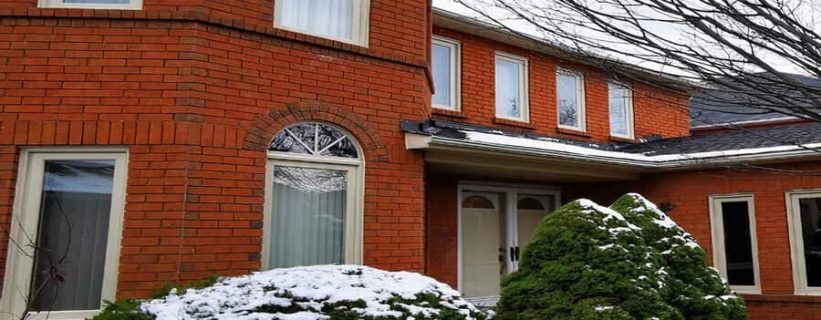Red brick house with snowy shrubs.