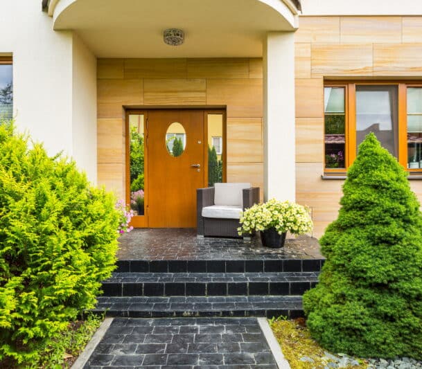 Wood-finish entry door with oval glass insert and matching wood-framed windows on a modern stone-clad home exterior in Prince Rupert, BC — HTR Windows and Doors