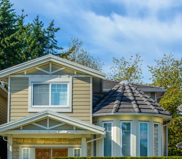White casement and bay windows on a beige-sided two-storey home with decorative gable trim in Kitimat, BC — HTR Windows and Doors