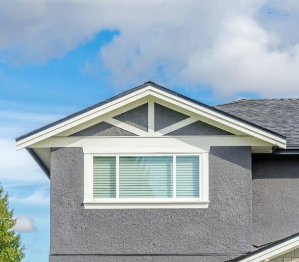 Wide white-framed picture window installed in the upper gable of a grey stucco home in Kitimat, BC — HTR Windows and Doors