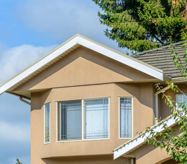 White sliding windows with vertical blinds installed on the upper storey of a tan stucco home in Kitimat, BC — HTR Windows and Doors