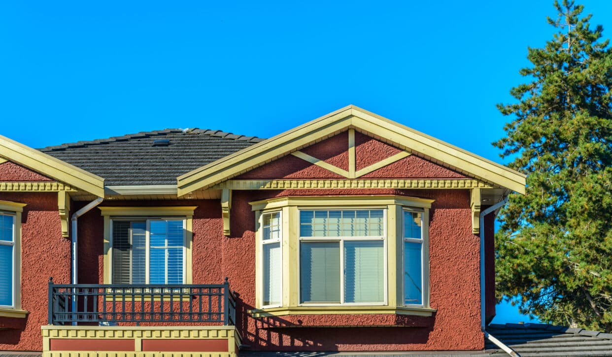 Replaced bay and casement windows with cream trim on a red stucco home upper storey in Prince Rupert, BC — HTR Windows and Doors